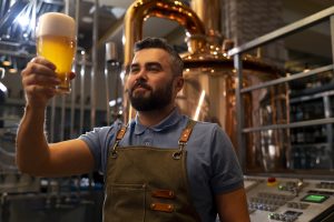 homem segura e observa cerveja artesanal dentro da fábrica